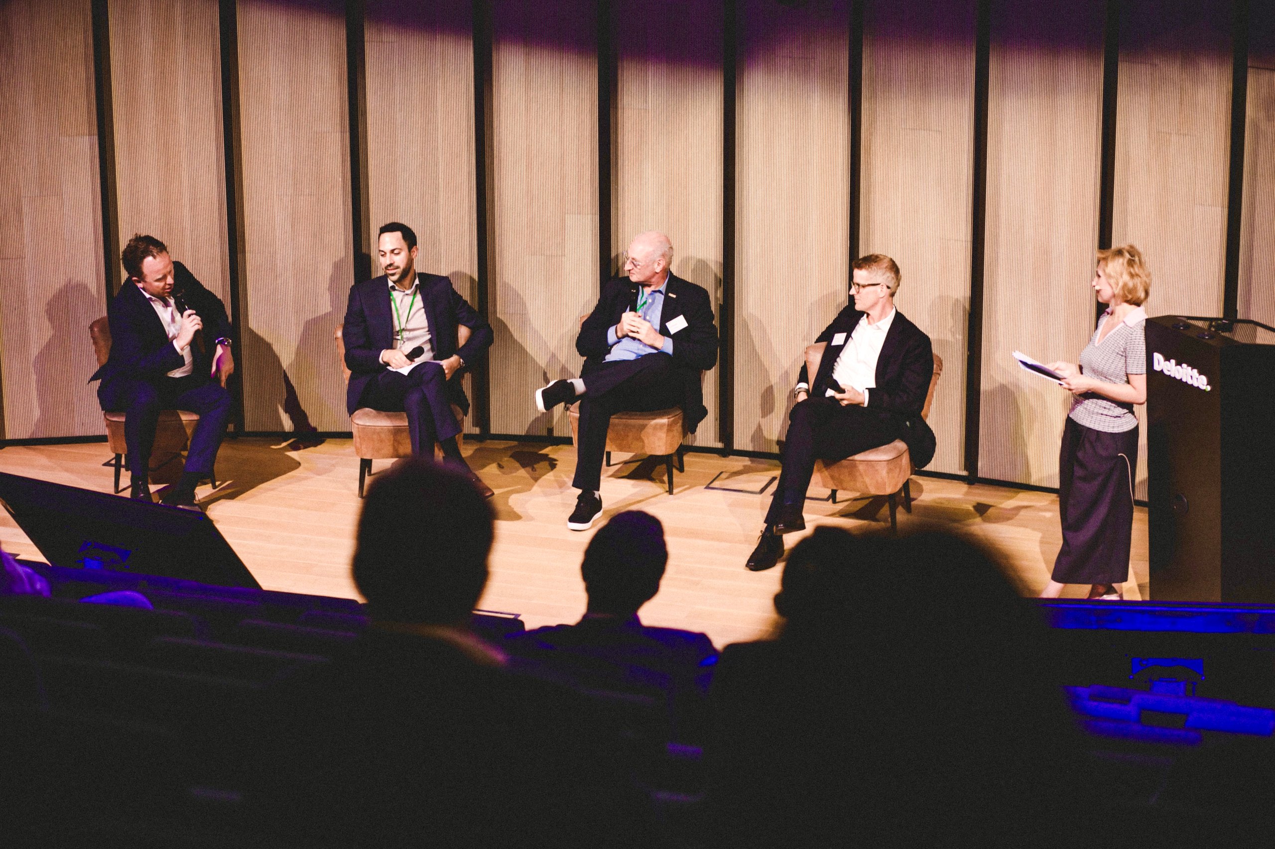 Five panelists sit onstage in front of striped acoustic panels during a discussion.